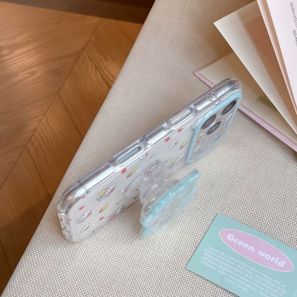 Side view of a Hello Kitty iPhone Case. The phone is propped up by a Hello Kitty pop socket on a textured beige surface.