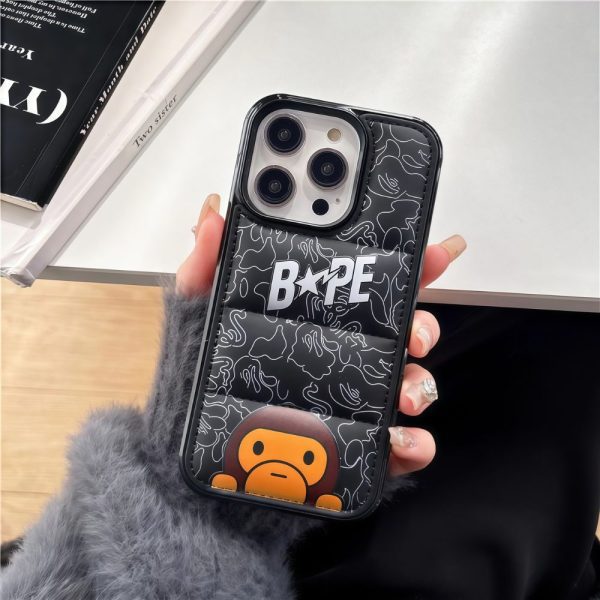 A puffer iPhone case with BAPE baby milo design in the hands of a woman in a velvet jacket with a table in the background