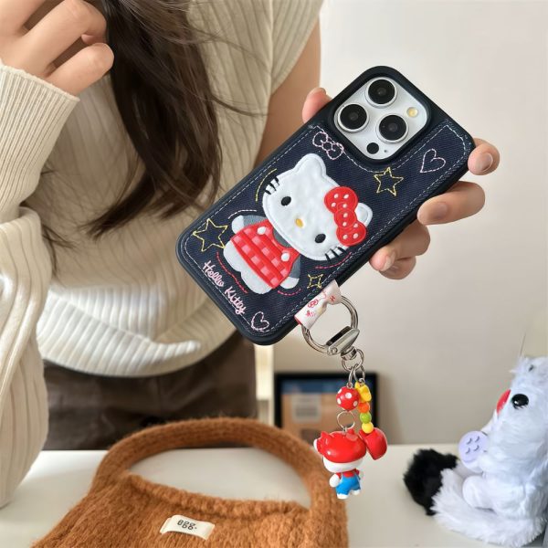 A three-quarter view from above of a hand holding the Hello Kitty Embroidered iPhone case. The user is wearing a beige tweed-like jacket.