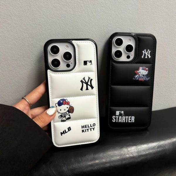 Two Hello Kitty baseball-themed puffer iPhone cases in black and white with a quilted padded design, featuring kawaii Hello Kitty artwork dressed as a baseball player, sporty NY-inspired logos, stitched leather texture, and raised camera protection displayed on a dark surface.